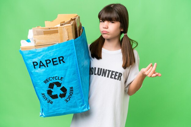 Menina caucasiana segurando um saco de reciclagem cheio de papel para reciclar sobre fundo isolado fazendo gesto de dúvidas enquanto levanta os ombros