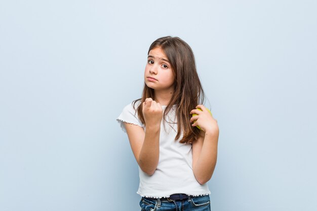 Menina caucasiana segurando uma maçã verde, apontando com o dedo para você, como se estivesse convidando para se aproximar.