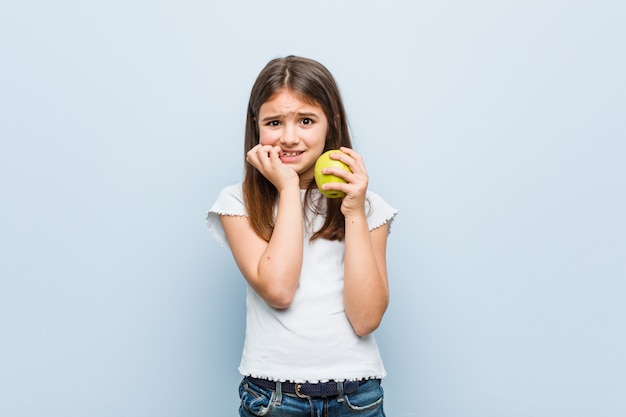 Menina caucasiana segurando uma maçã verde, roer unhas, nervosas e muito ansiosas.