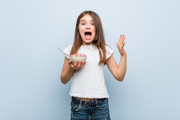 Menina caucasiana segurando uma tigela de cereais comemorando uma vitória ou sucesso