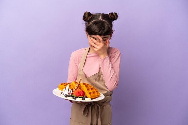 Foto menina caucasiana segurando waffles isolados em um fundo roxo rindo