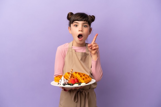 Menina caucasiana segurando waffles isolados na parede roxa com a intenção de descobrir a solução enquanto levanta um dedo