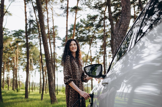 Menina caucasiana sorridente, conectando o cabo de eletricidade em veículo elétrico para carregar no shopping ensolarado, foco seletivo, estilo de vida e conceito de ecologia