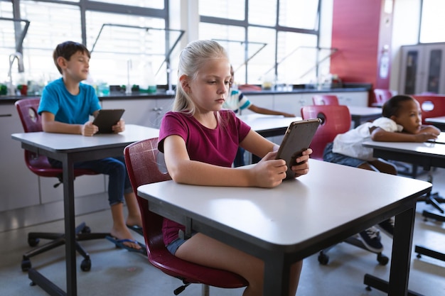 Menina caucasiana usando tablet digital enquanto está sentado em sua mesa na classe na escola