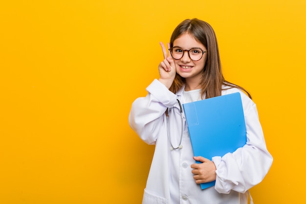 Menina caucasiana vestindo traje médico sorrindo e levantando o polegar