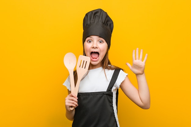 Menina caucasiana vestindo uma fantasia de chef, comemorando uma vitória ou sucesso