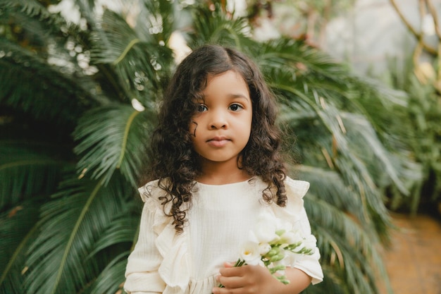 Menina cercada por folhas tropicais Retrato de uma criança morena com cabelos escuros Cosméticos naturais saúde limpeza