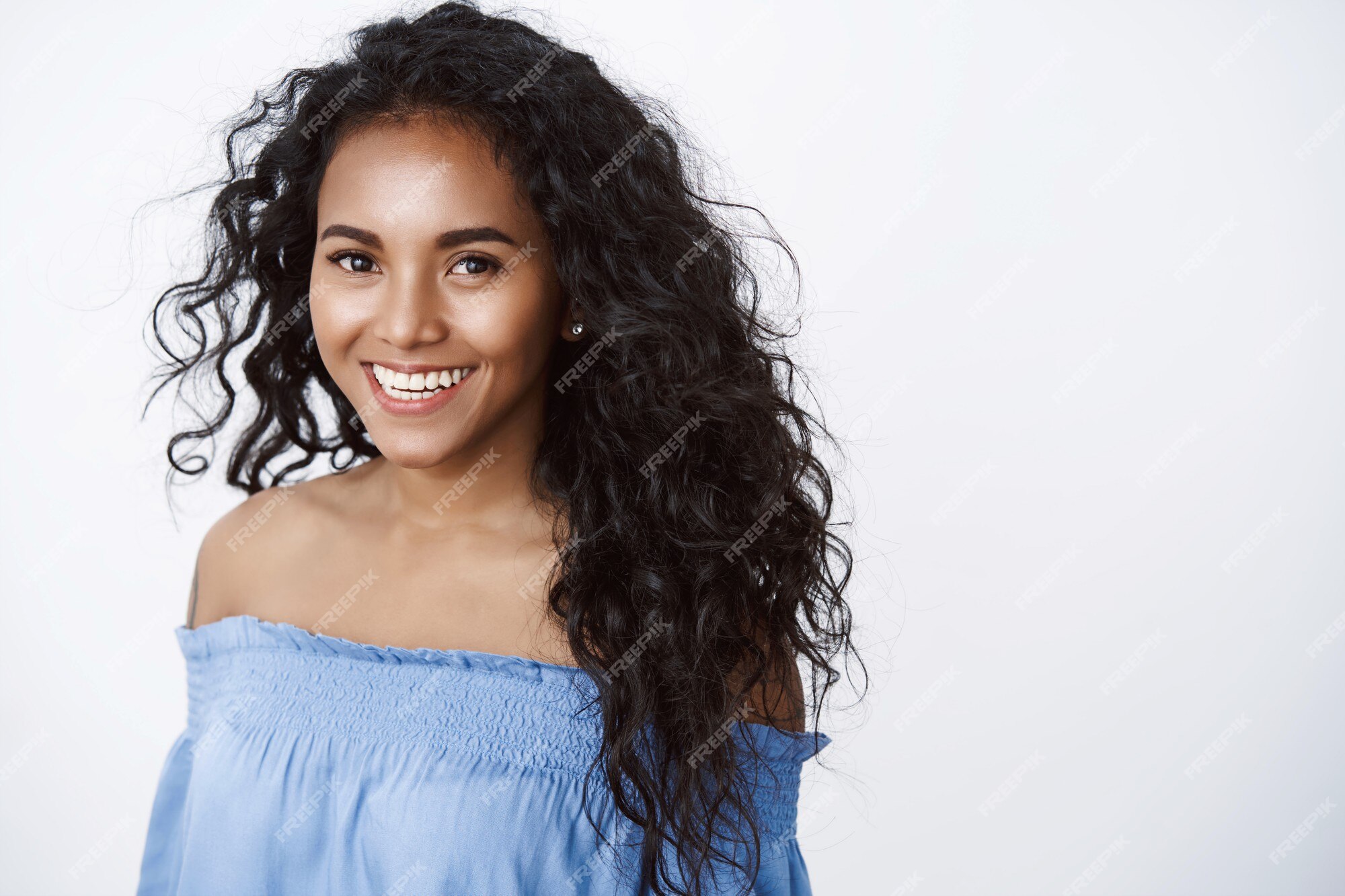 Menina charmosa de cabelos cacheados em blusa azul sorrindo alegremente, o  olhar com uma expressão feliz e terna