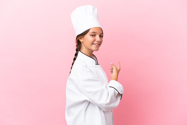 Menina chef caucasiana isolada em um fundo rosa apontando para trás