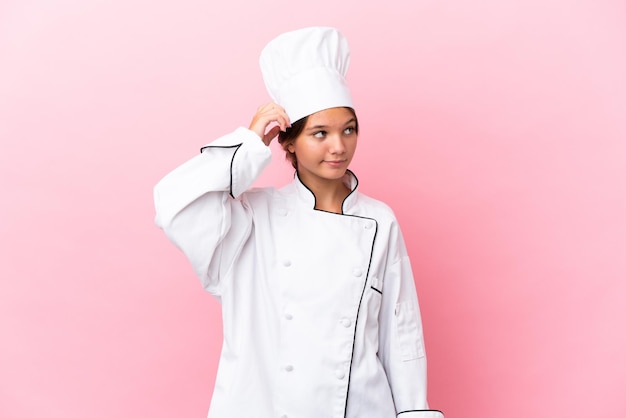 Menina chef caucasiana isolada em um fundo rosa com dúvidas e expressão confusa