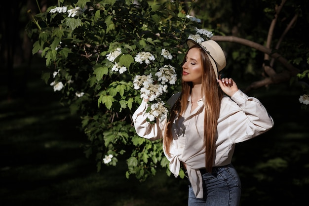 Menina cheira flores brancas em um parque de verão. pele saudável.