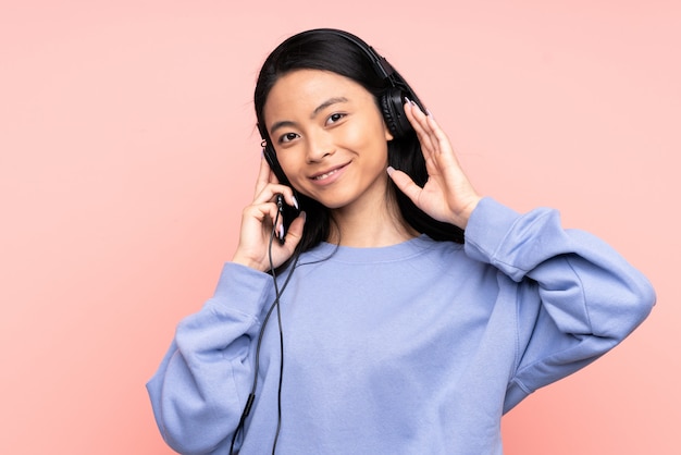 Menina chinesa adolescente na parede rosa ouvindo música