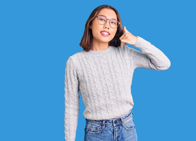 Menina chinesa bonita vestindo roupas casuais sorrindo fazendo gesto de telefone com a mão e os dedos como falar ao telefone. comunicar conceitos.