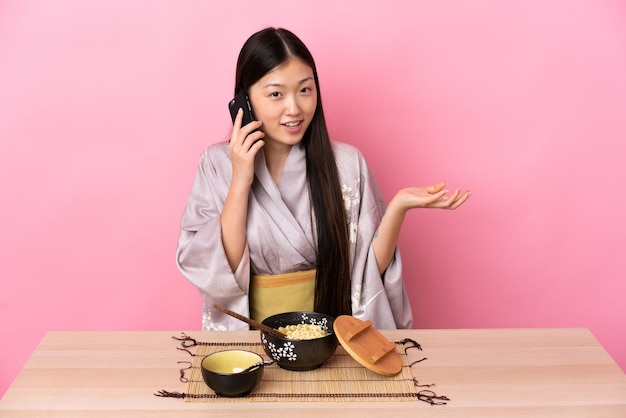 Menina chinesa de quimono, comendo macarrão, conversando com alguém ao telefone celular