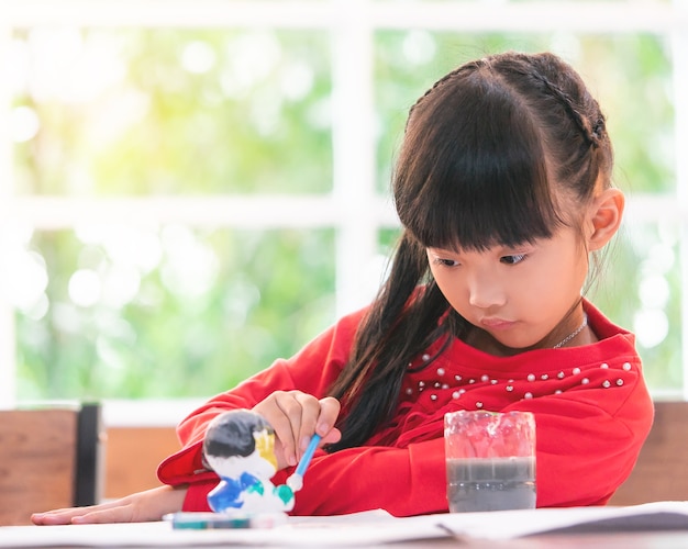 Menina chinesa está pintando uma boneca em sala de aula