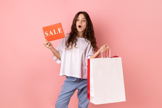 Foto menina chocada segurando sacolas de compras e cartão de venda surpresa com grandes descontos de férias