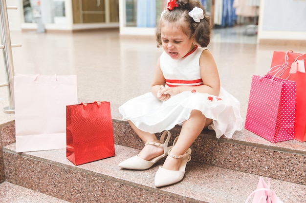 Menina chorando no shopping com sacolas coloridas