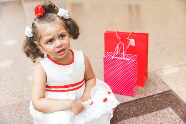 Menina chorando no shopping com sacolas coloridas