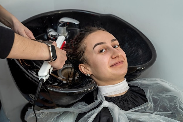 menina cliente muito elegante sorri em um salão de beleza quando sua cabeça é lavada por um mestre profissional. Conceito de mulher feliz em tratamentos de beleza