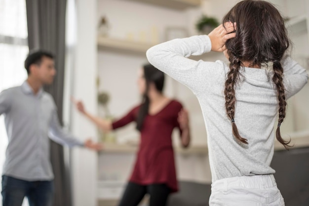 Foto menina cobrindo as orelhas enquanto os pais discutem em casa