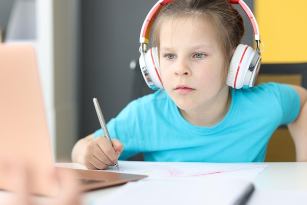 Menina colegial em fones de ouvido sentado na frente do laptop em casa