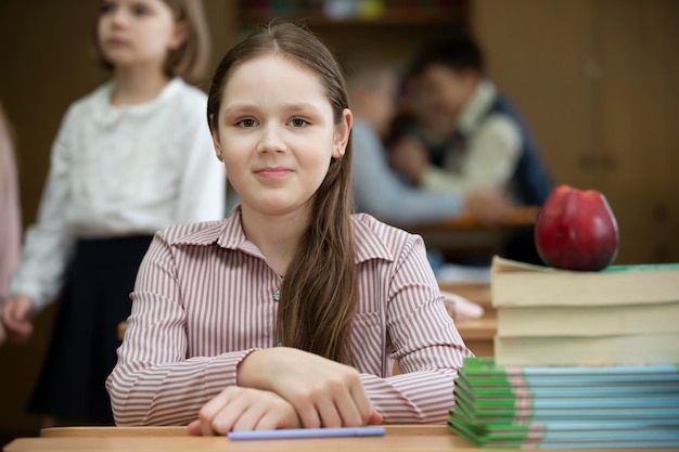 Menina colegial na mesa Menina na sala de aula com livros e uma maçã