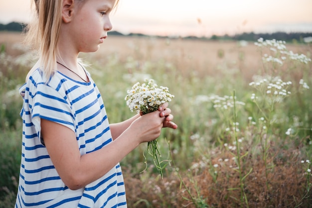 Menina colhendo flores silvestres no campo de trigo amarelo na paisagem do pôr do sol de verão, fundo agrícola de verão com espigas de trigo maduras