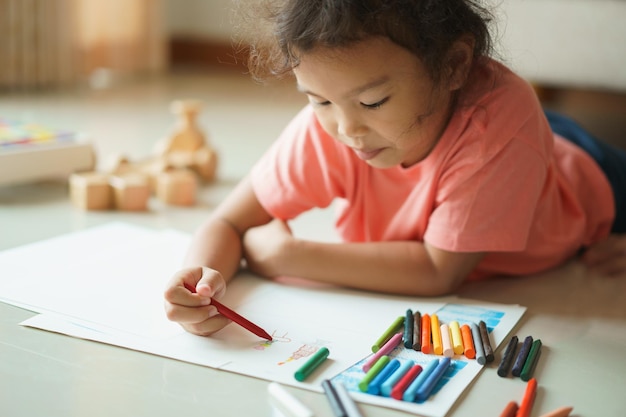 Menina colorindo papel enquanto está deitada em casa