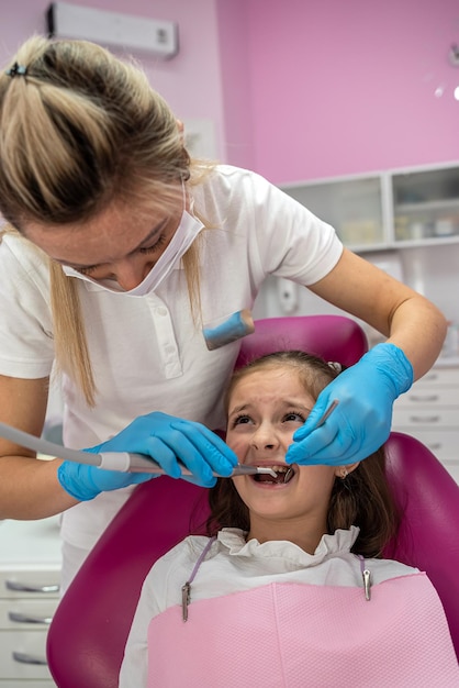 Foto menina com a boca aberta olhando para o dentista enquanto o médico verifica os dentes da criança