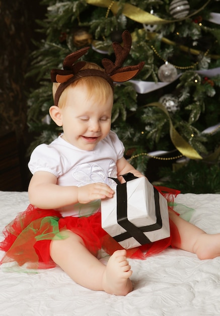 Menina com a caixa de presente perto de árvore de Natal de decoração. Tempo feliz.