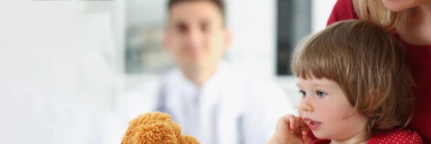 Foto menina com a mãe brincando com o ursinho de pelúcia antes da consulta médica