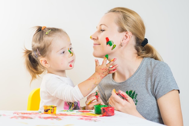 Menina com a mãe brincando e brincando com tintas coloridas