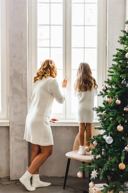 Menina com a mãe em pé na janela, interior é decorado para o Natal