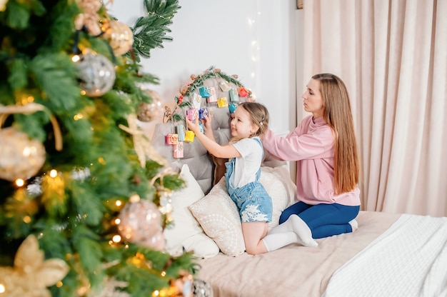 Menina com a mãe examinando presentes no calendário do advento