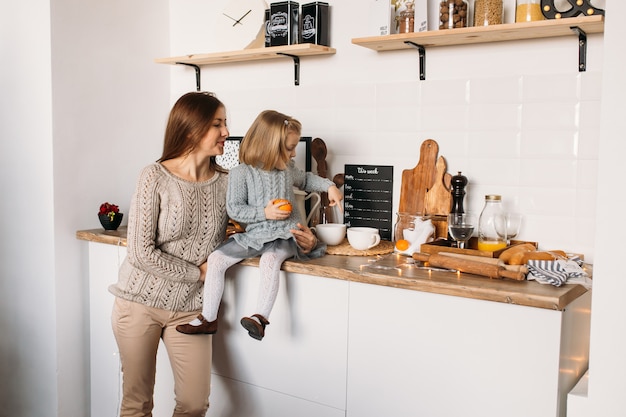 Menina com a mãe na cozinha em casa.