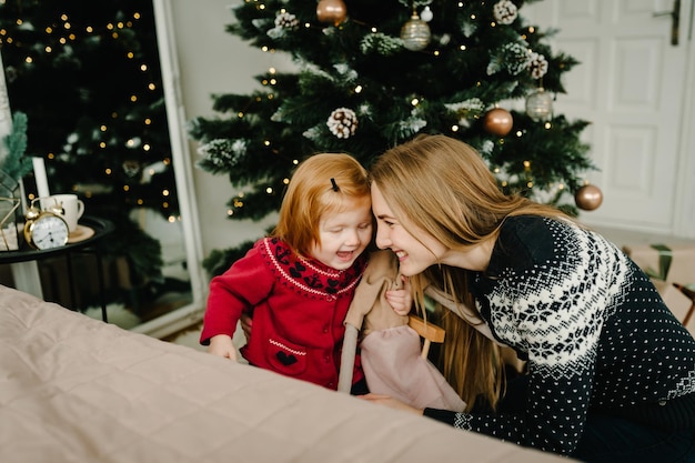 Menina com a mãe no chão perto da árvore de Natal Feliz Ano Novo e Feliz Natal Interior decorado de Natal O conceito de férias em família