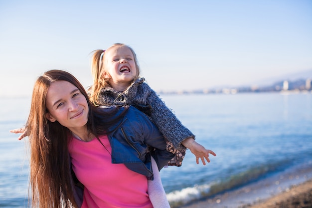 Menina com a mãe se divertindo na praia em um dia de inverno