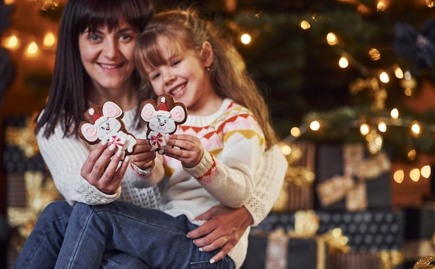 Menina com a mãe segurando biscoitos de natal nas mãos.