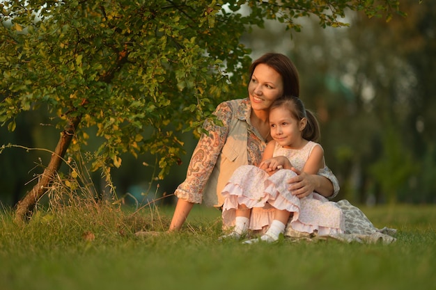 Menina com a mãe sentada sob uma árvore na natureza ao pôr do sol