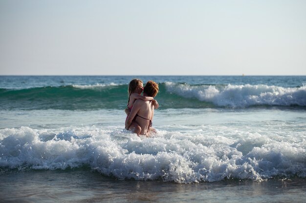 Menina com a mãe tomando banho nas ondas do oceano