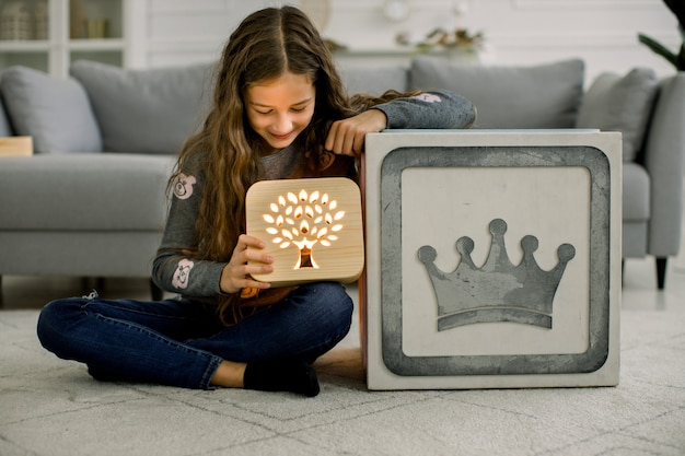 Menina com abajur de madeira sentado na moderna e aconchegante sala de estar leve em casa.