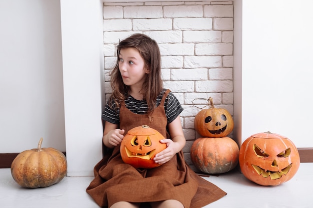 Menina com abóbora esculpida no halloween em casa sentada perto da lareira