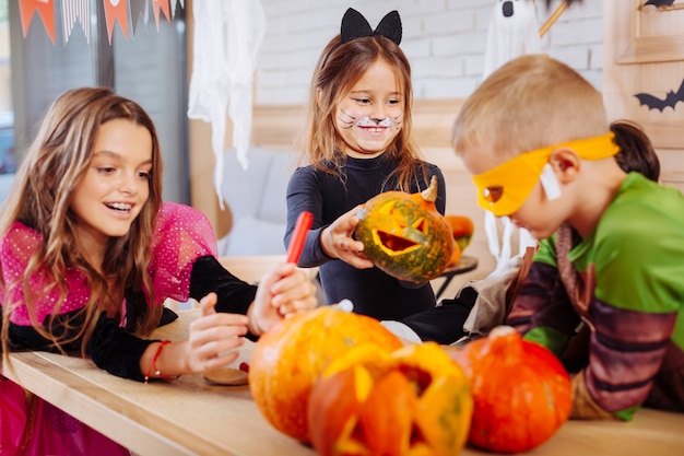 Menina com abóbora. linda garota sorridente usando fantasia de gato e se sentindo animada enquanto segura uma pequena abóbora de halloween esculpida