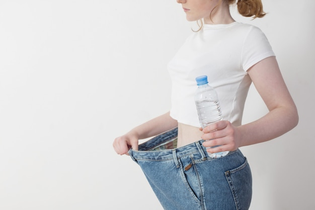 Menina com água na garrafa, puxando seus jeans grandes e mostrando a perda de peso