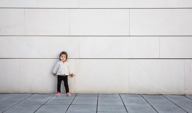 Menina com aparência esportiva posando em frente a uma parede de pedra branca moderna