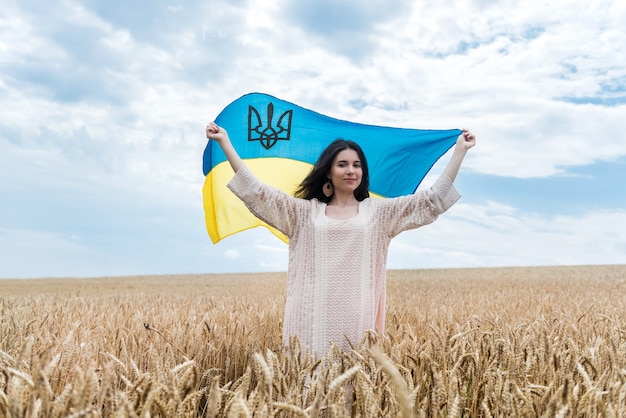 Menina com bandeira da ucrânia e caminha por um campo de trigo maduro