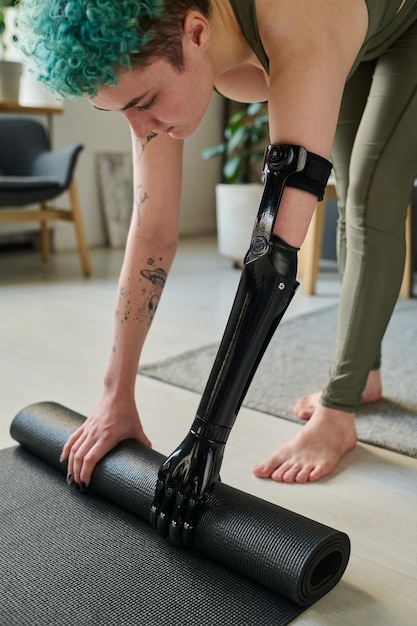 Foto menina com braço protético usando colchonete para treinamento esportivo em casa