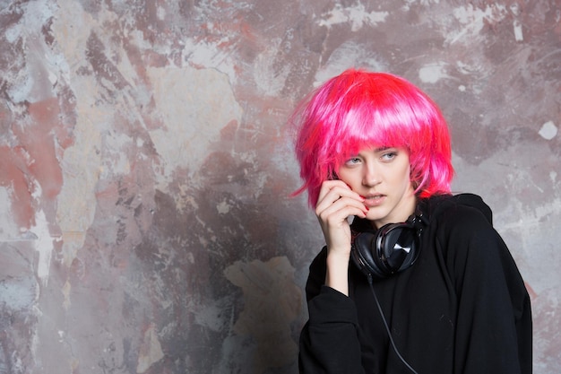 Menina com cabelo artificial brilhante no fone de ouvido. Salão de cabeleireiro e barbearia. DJ de música e festa. Beleza e moda. Mulher de peruca rosa com fones de ouvido musicais, copie o espaço