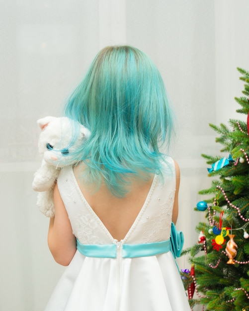 Menina com cabelo azul em um vestido branco e um gato de brinquedo