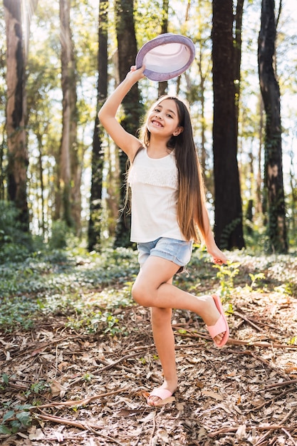 Menina com cabelo comprido, segurando um chapéu ao ar livre - retrato de uma linda menina, sorrindo alegremente.